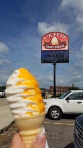 White & Orange Soft-Serve Ice Cream Cone being held up in front on a 4 Queens Ice Cream Street Sign