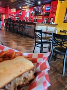 Sandwich in a red & white checkered basket with a restaurant barn in the background