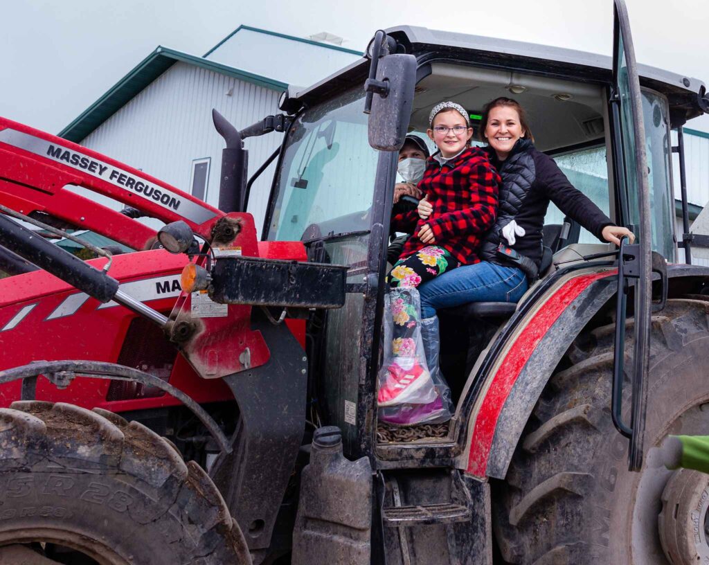 A mom and a daughter in a tractor with the door open smiling